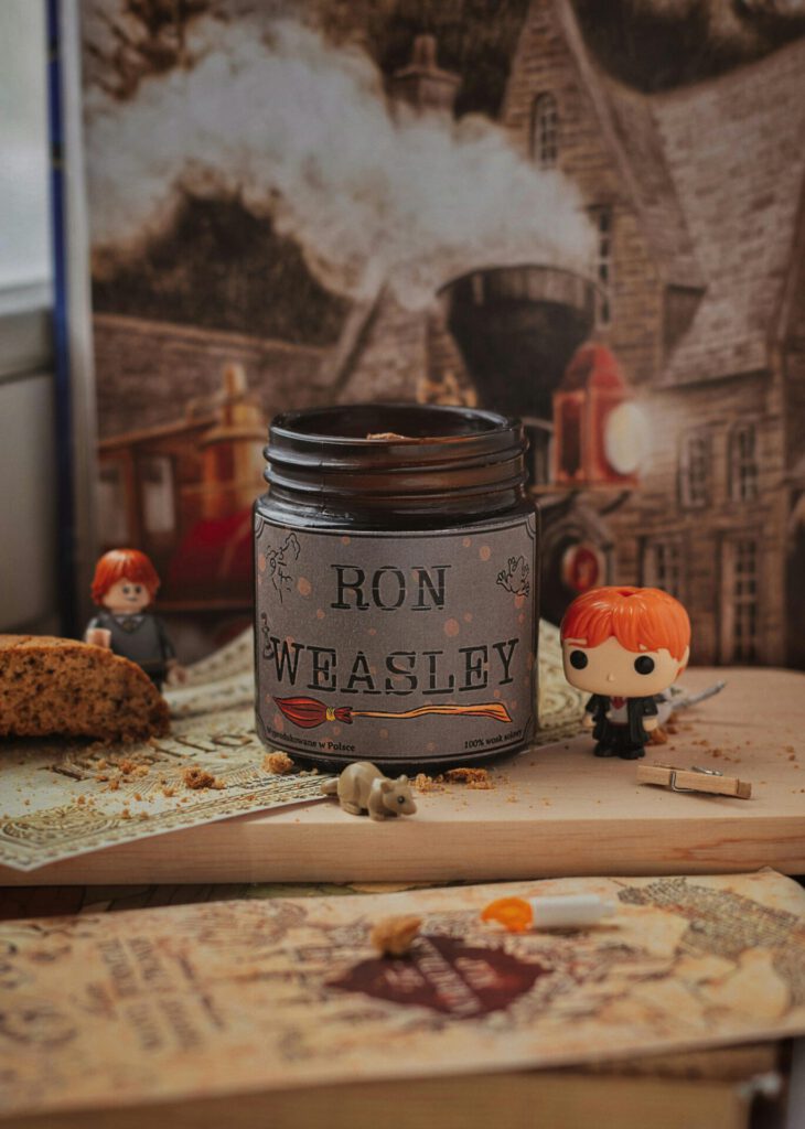 Still life of Ron Weasley funko pops with a themed candle and Hogwarts backdrop.