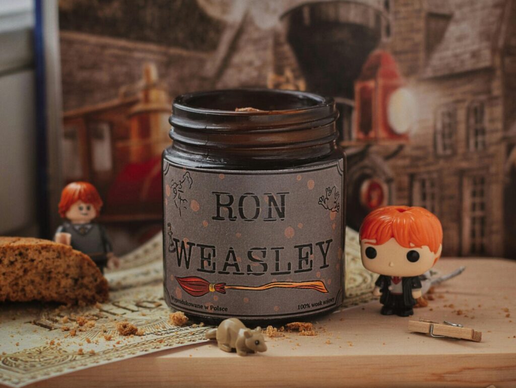 Still life of Ron Weasley funko pops with a themed candle and Hogwarts backdrop.