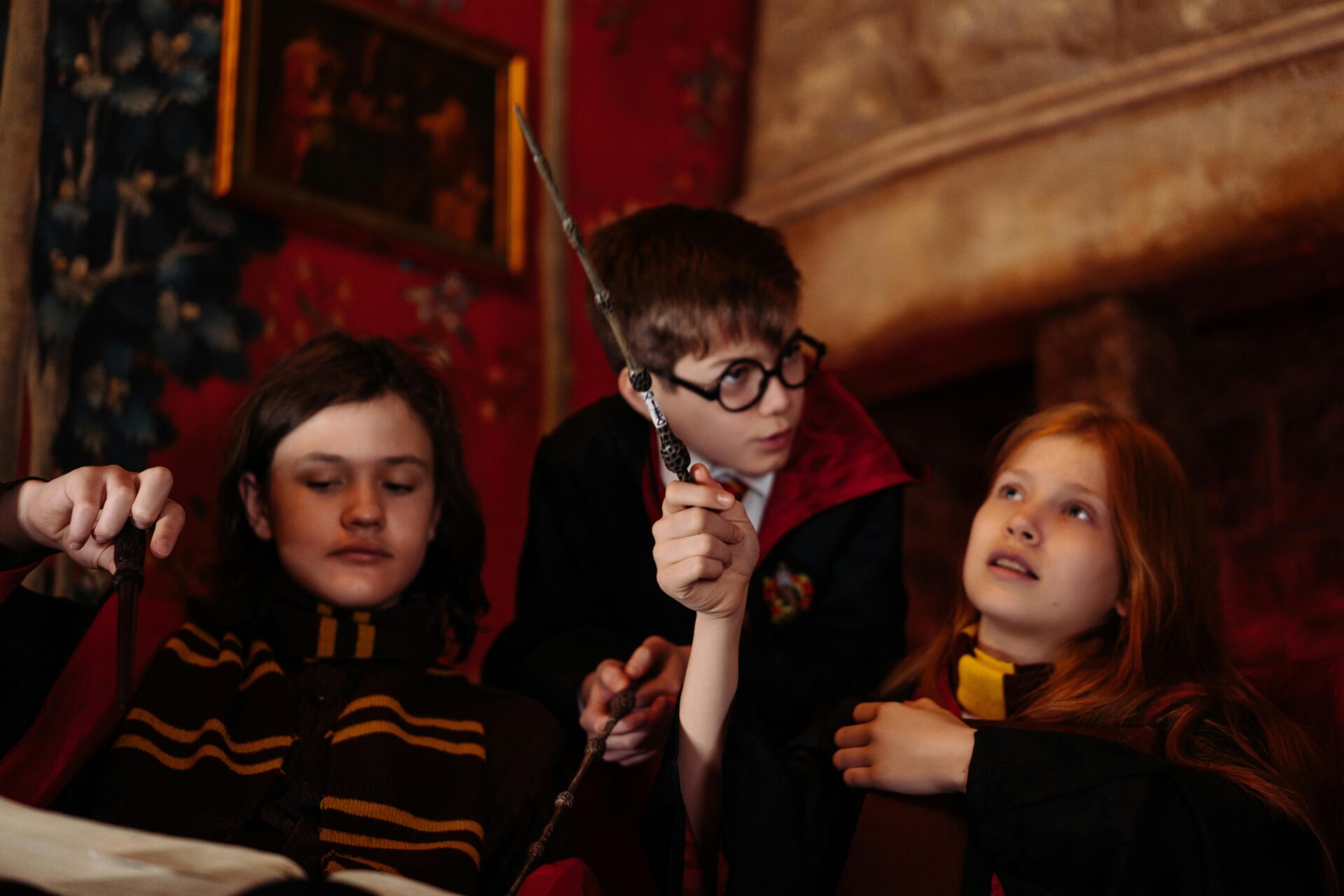 Three children dressed as wizards and witches role-playing with wands in a cozy indoor setting.